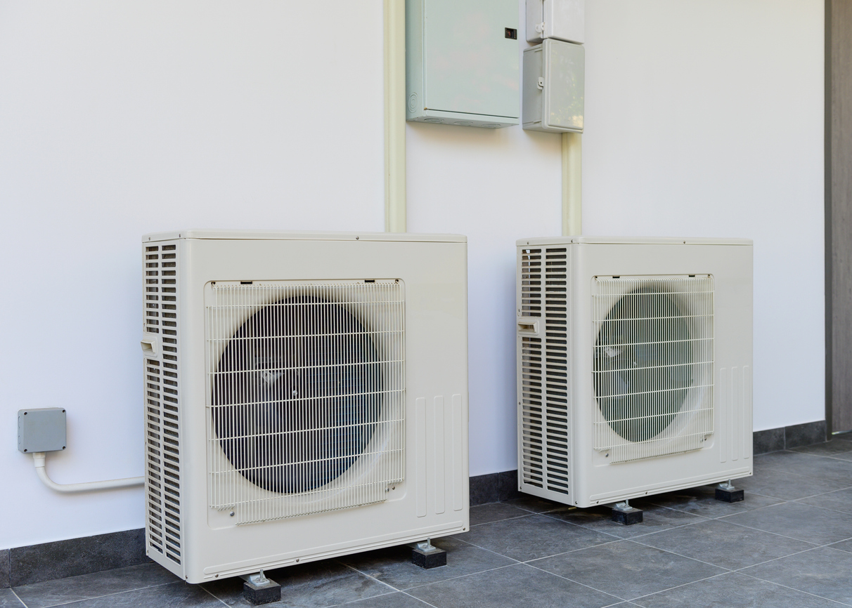 Two outdoor air conditioning units installed on a wall with electrical connections visible.