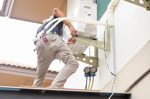 Technician installing a new air conditioning unit outdoors, with gauges attached to the system.