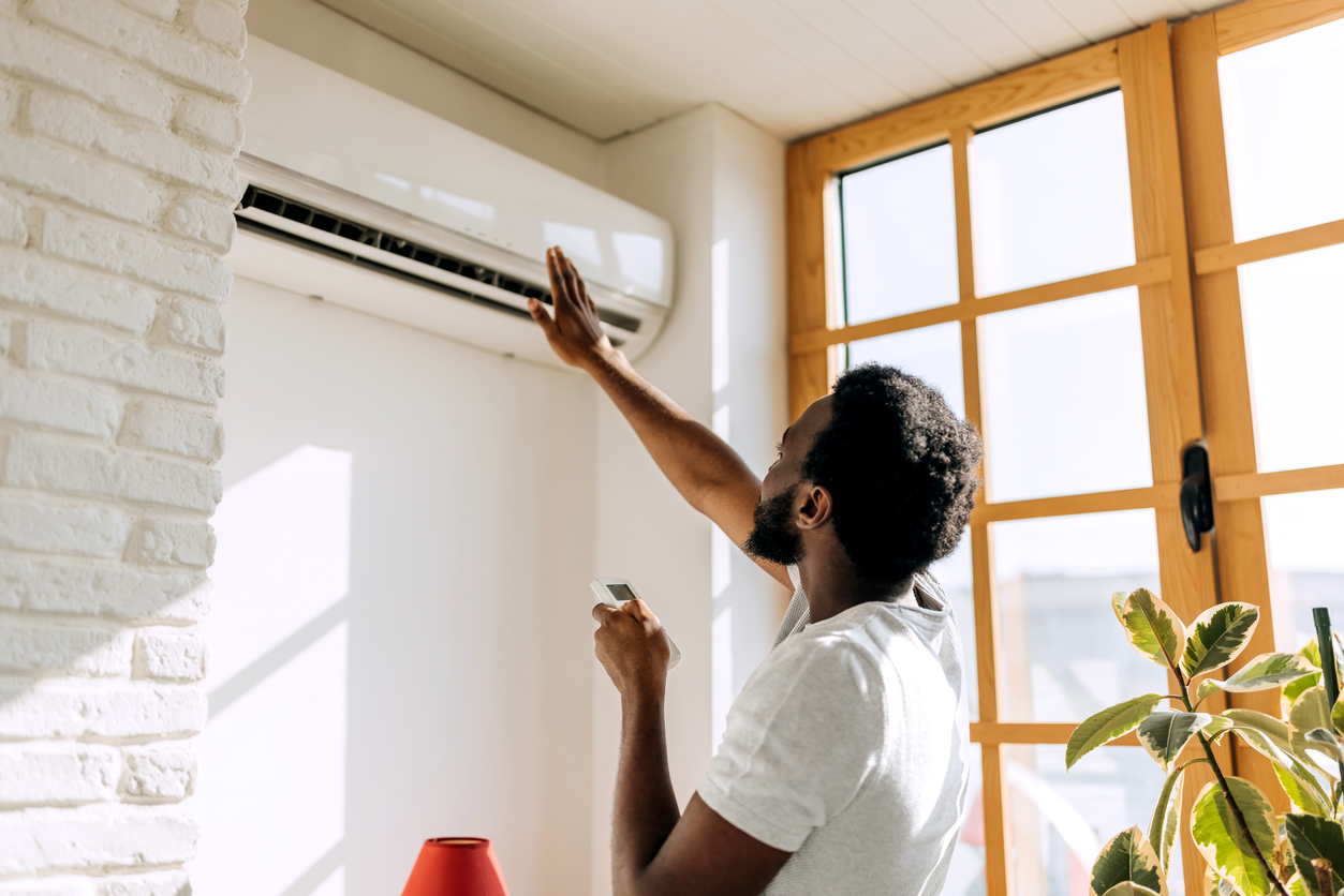 Man checking a wall-mounted air conditioner at home while troubleshooting why the AC is blowing hot air.