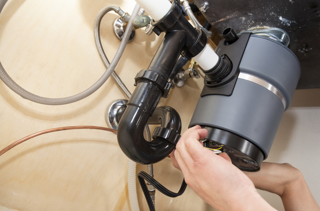 Plumber installing garbage disposal under sink in Atlanta home.