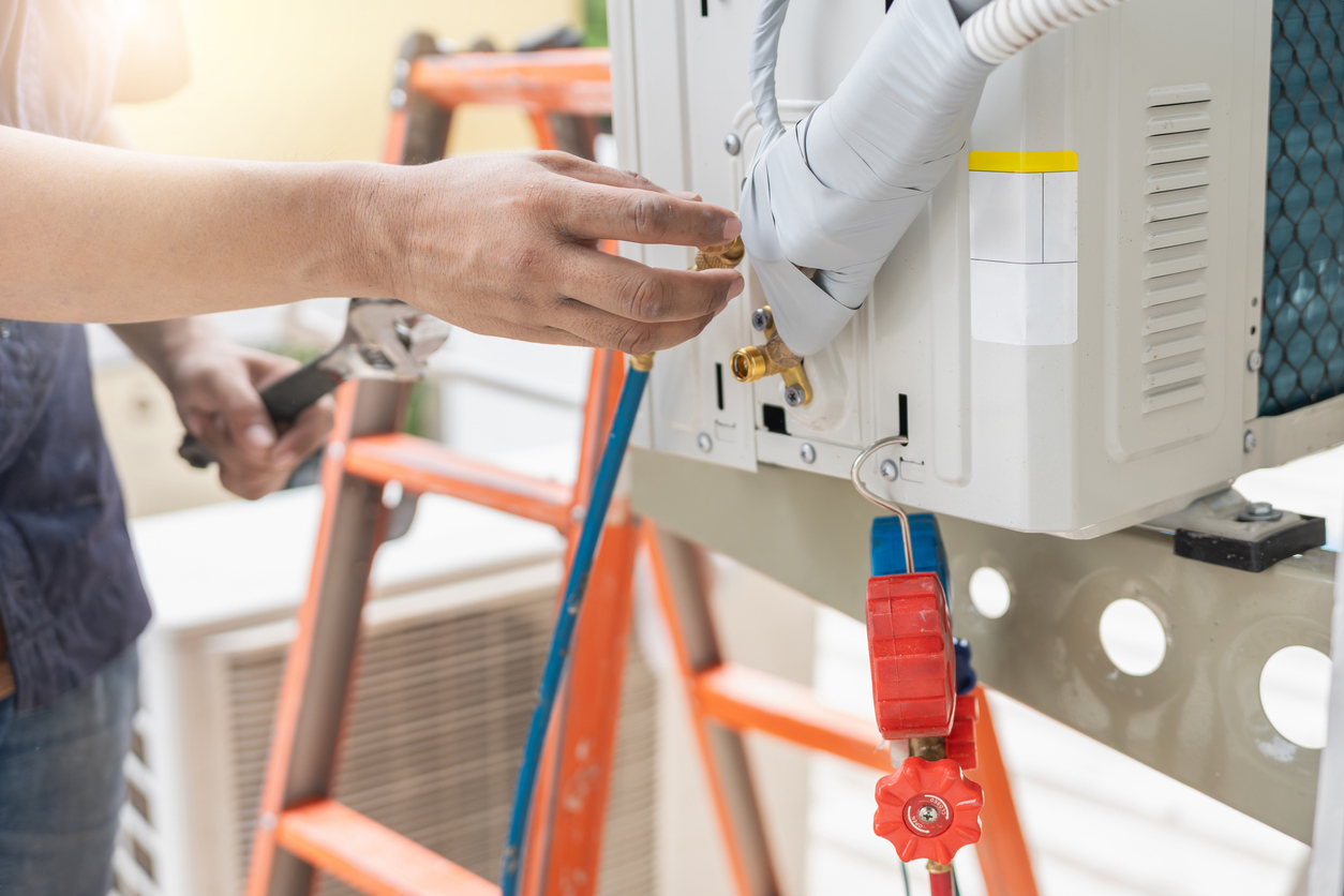  Allgood HVAC technician connecting refrigerant lines to an outdoor air conditioning unit during replacement.